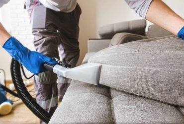 Man dry cleaner's employee hand in protective rubber glove cleaning sofa with professionally extraction method. Early spring regular cleanup. Commercial cleaning company concept. Closeup
